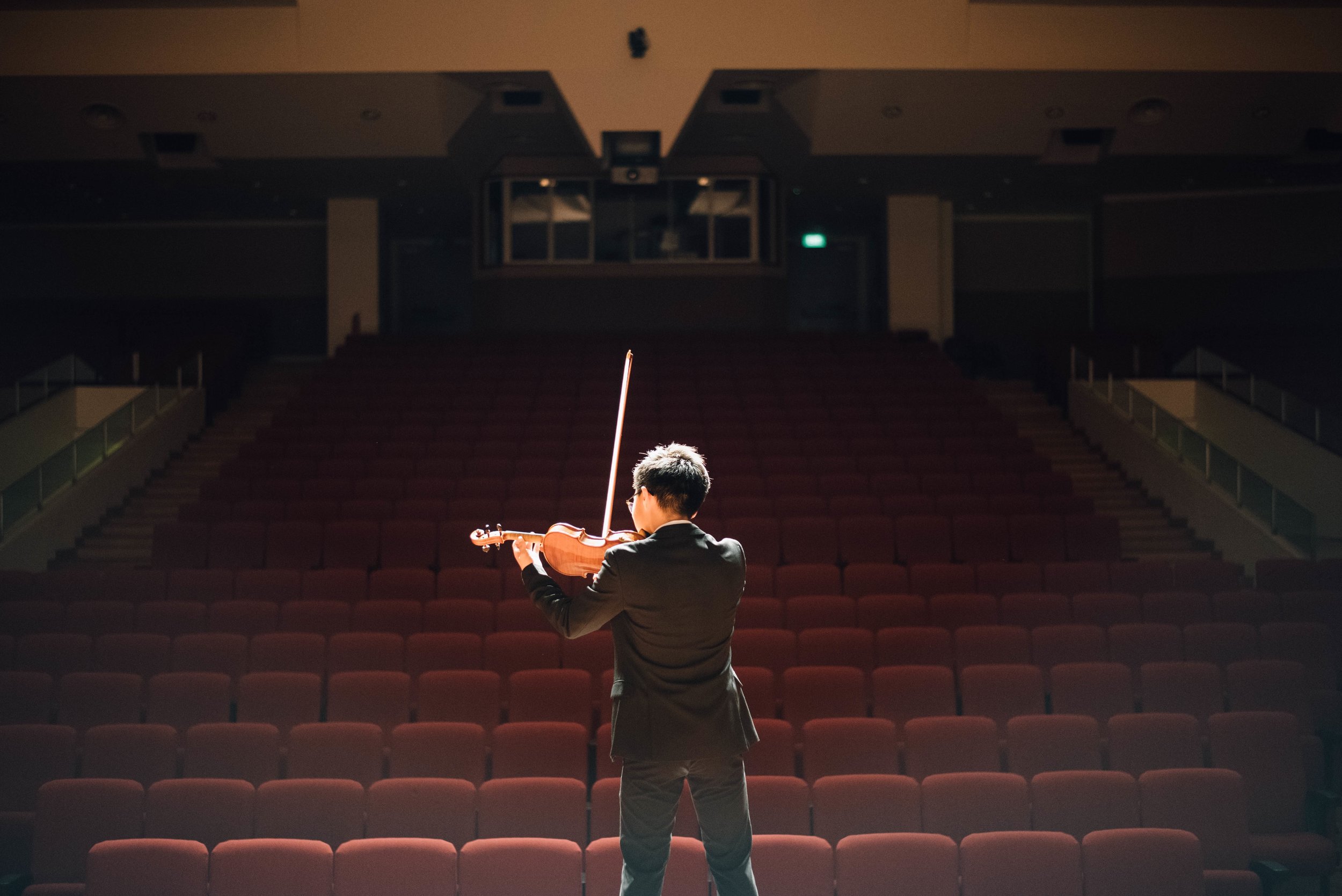 A person playing the violin in an empty auditorium.