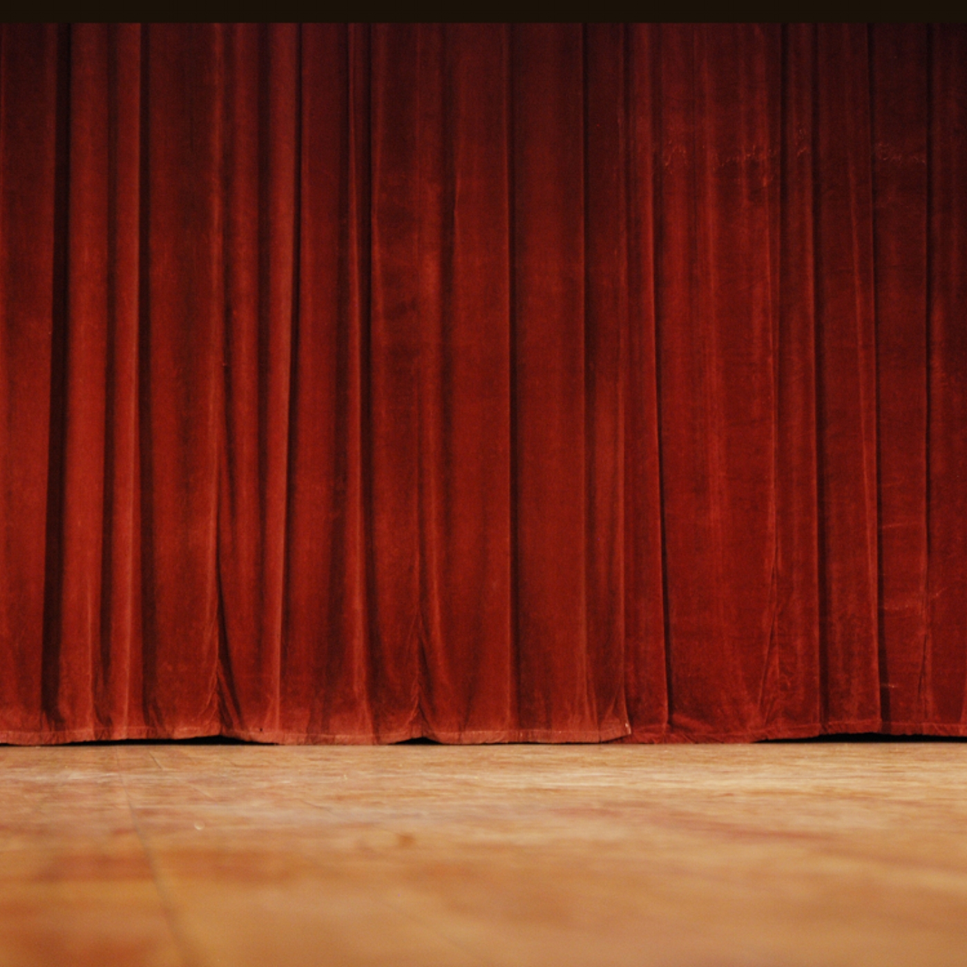 A stage with a red velvet curtain and a wooden floor.